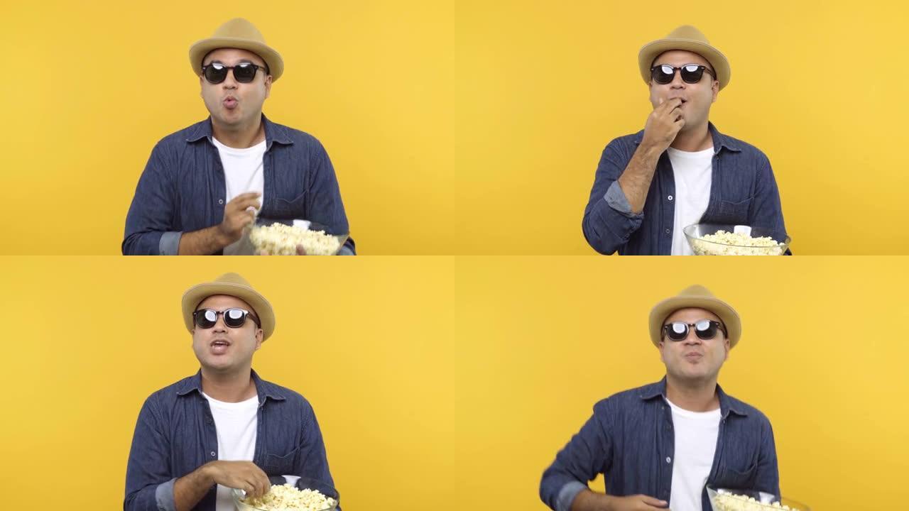 一名男子戴着眼镜吃爆米花，一边看一场运动反应兴奋、有趣、支持，孤立在黄色背景上。