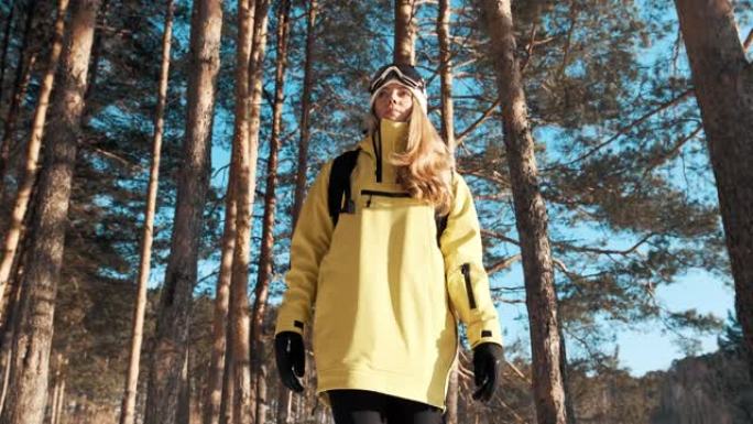 一个穿着黄色夹克，背着背包和滑雪板面具的女孩穿过森林