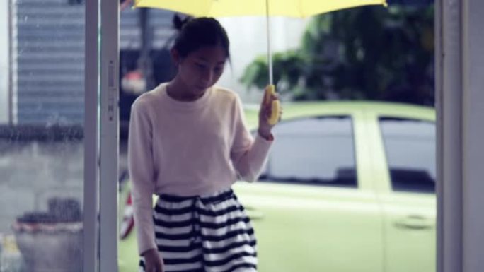 亚洲女孩在雨天在房子前使用黄色雨伞，生活方式概念。
