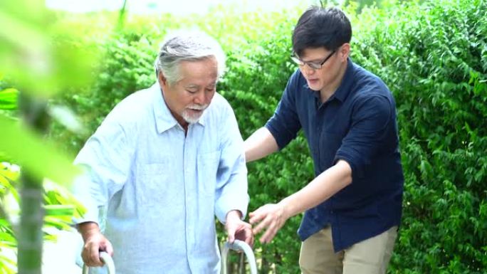 老年亚洲父亲和成年儿子在后院散步。积极的亚洲男子护理人员帮助患者