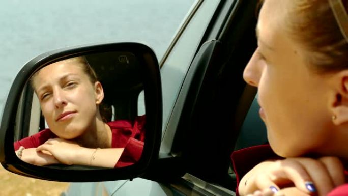 忧郁的年轻女子在海岸上的汽车中戴着墨镜