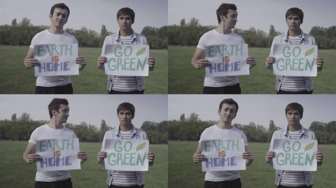 两名积极认真的男性志愿者举着海报地球是家，走向绿色，看着相机。自信的年轻白人男子宣传环境保护的肖像。