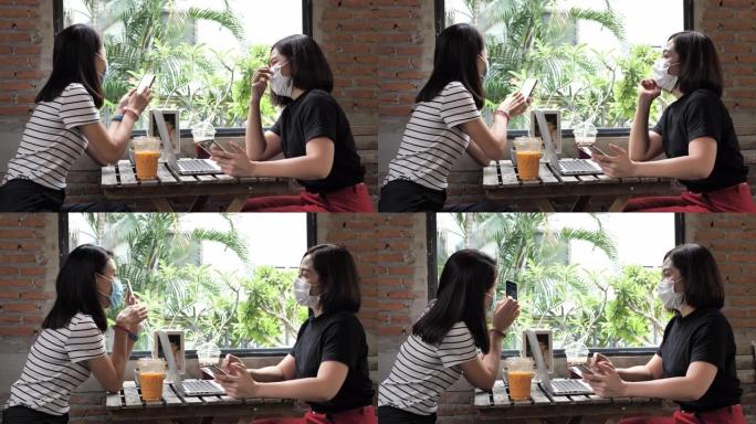 两个亚洲女性最好的朋友戴着医疗脸马克，喜欢在舒适的咖啡店里用笑脸见面交谈