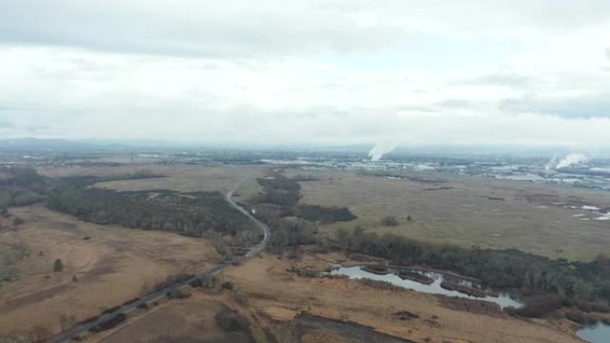 4k鸟瞰图飞越绿色田野，朝带有烟囱的工业区飞去