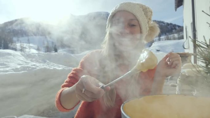 快乐的年轻女子在瑞士吃奶酪火锅，享受阿尔卑斯山和白雪皑皑的山脉