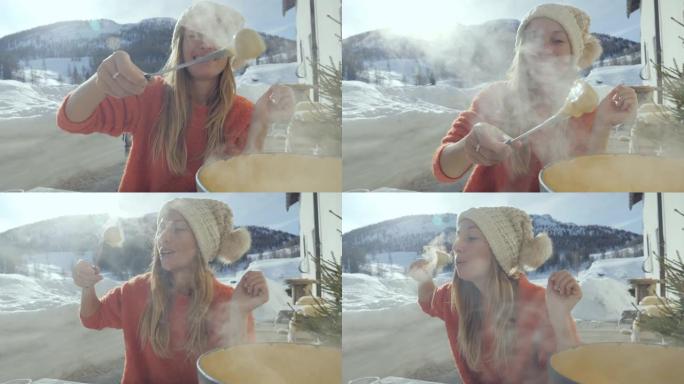 快乐的年轻女子在瑞士吃奶酪火锅，享受阿尔卑斯山和白雪皑皑的山脉