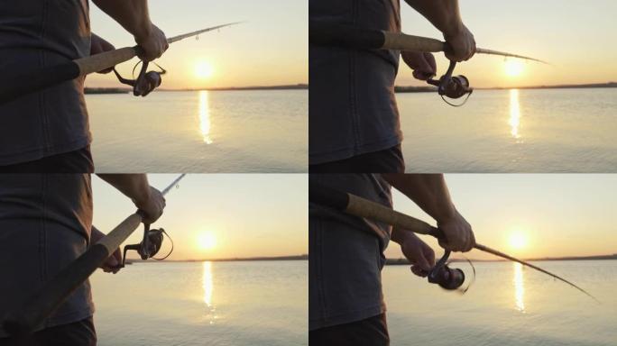 用钓鱼竿的卷轴处理旋转，以对抗橙色日落慢动作。男子业余爱好在海上钓鱼收紧了鱼线卷轴的夏天。镜头光斑。