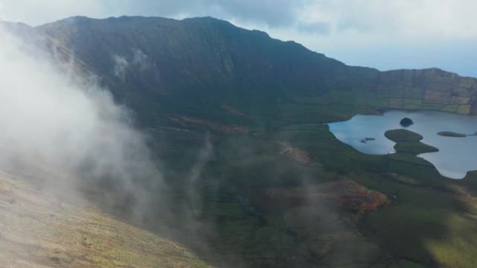 飞越火山顶部的云层。火山口的绿色斜坡和湖泊。卡尔代拉奥、科尔沃、亚速尔群岛