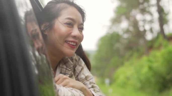 快乐年轻美丽的亚洲女性旅行者的慢动作坐在车里，在雨天把她的脸和手从车窗外拉出来。漂亮女孩享受户外生活