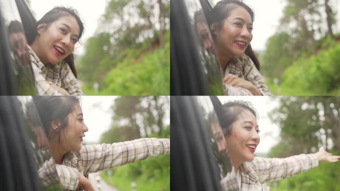 快乐年轻美丽的亚洲女性旅行者的慢动作坐在车里，在雨天把她的脸和手从车窗外拉出来。漂亮女孩享受户外生活