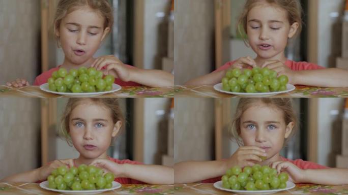 孩子吃甜葡萄。小女孩素食主义者正在吃盘子里的白葡萄，坐在厨房的餐桌上。健康的有机素食。水果收获。