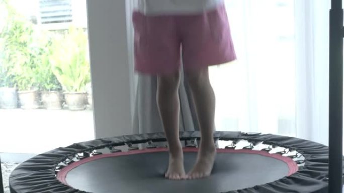 亚洲女孩在家里窗户附近的迷你蹦床上跳跃，运动概念。