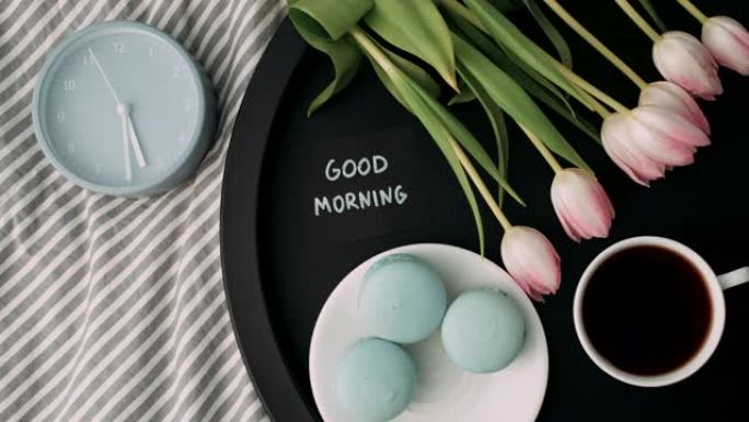 托盘上有法式马卡龙和新鲜郁金香的笔记 “早上好” 的俯视图，上午5:30点一杯咖啡和闹钟