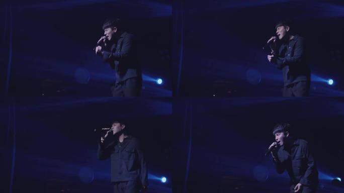 一位黑衣男歌手带着悲伤的心情唱歌，身后闪耀着蓝色的灯光，以黑暗为背景。
