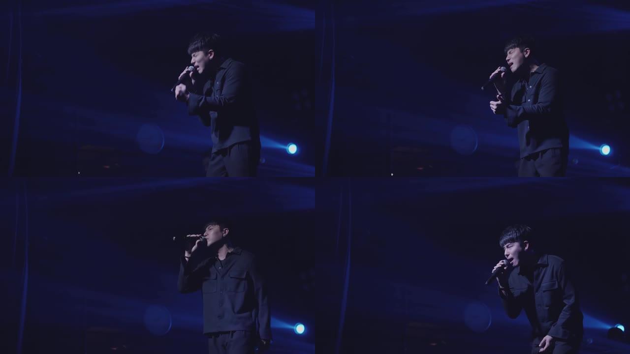 一位黑衣男歌手带着悲伤的心情唱歌，身后闪耀着蓝色的灯光，以黑暗为背景。