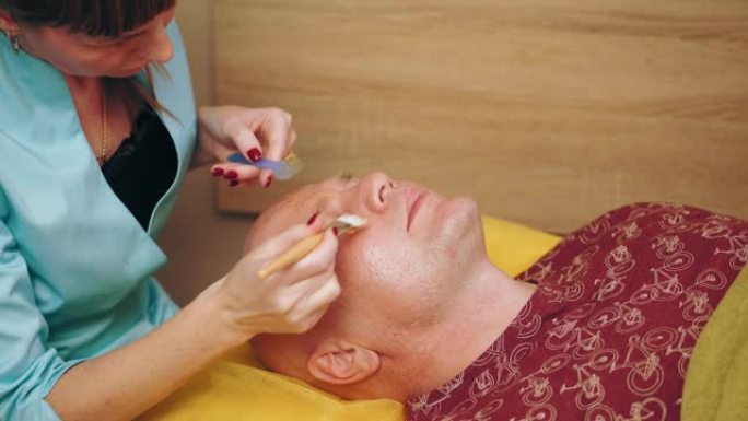 美容，男士洗脸。男性的整容手术。男人躺在沙发上，在美容诊所接受面部皮肤护理程序。皮肤护理皮肤科治疗