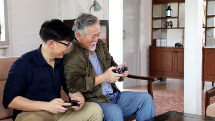 退休年龄的亚洲高级男子与儿子在舒适的家中玩视频游戏机