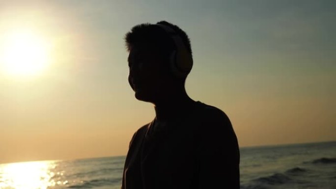 剪影男孩早上在海滩上戴着耳机，慢动作。