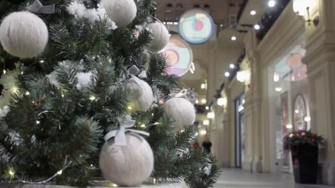 在商店橱窗的背景下，一棵装饰有毛线球的圣诞树站在购物中心的大厅里