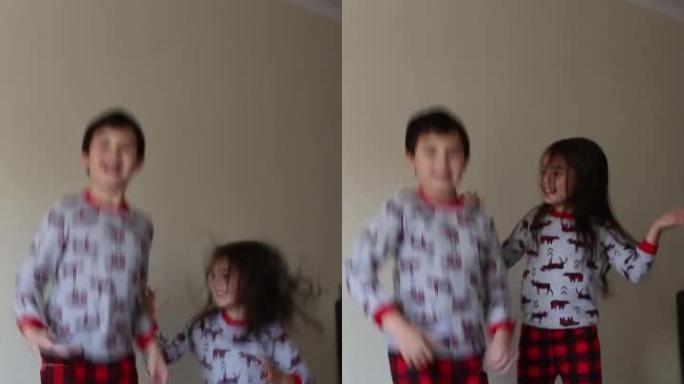 幸福的家庭，可爱的兄妹黑发女郎穿着红色睡衣在床上跳跃，早上在家玩得开心