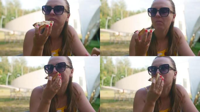 年轻女孩拿一片肉披萨，夏天在户外吃。