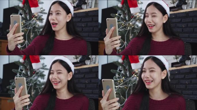 年轻的亚洲女性在圣诞节那天与朋友在家里通过电话与朋友进行在线自拍视频通话，社交距离，新常态，智能手机