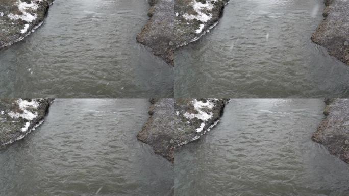 在阴沉的冬日，河上正在下雪。大片雪花落在水面上。天气不好。冬季景观。从顶部看。4K。