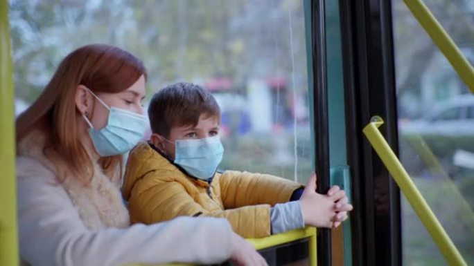 带着孩子乘坐公共汽车旅行，带着孩子戴着医用口罩的年轻女子遵循现代预防措施，以防止社会病毒和感染