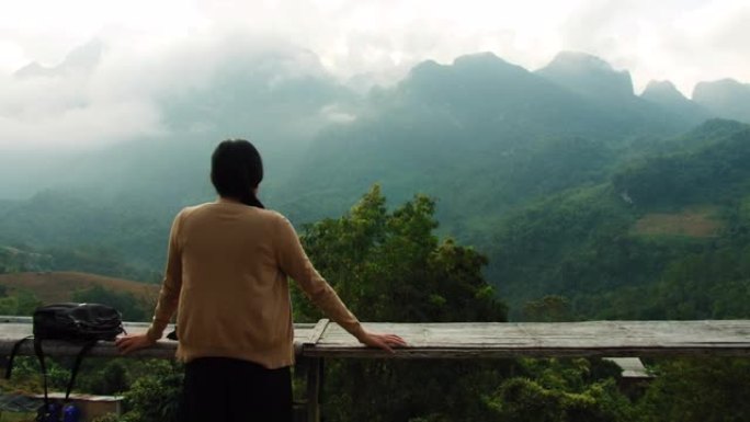 亚洲妇女旅行并站在度假酒店的阳台上，可以欣赏到山脉，云彩，薄雾和美丽的天空背景。自然旅行的概念。4k