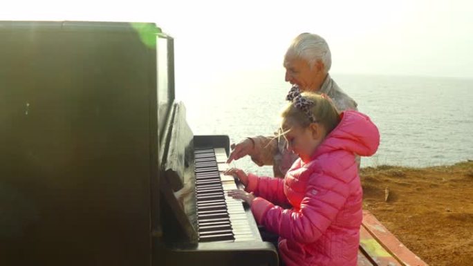 老人和小女孩在海边散步时一起弹旧钢琴