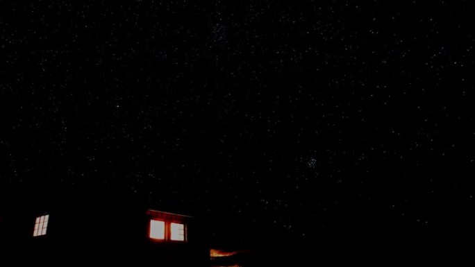 山里的小木屋，窗外闪耀着光芒，背景是繁星点点的夜空。延时视频。