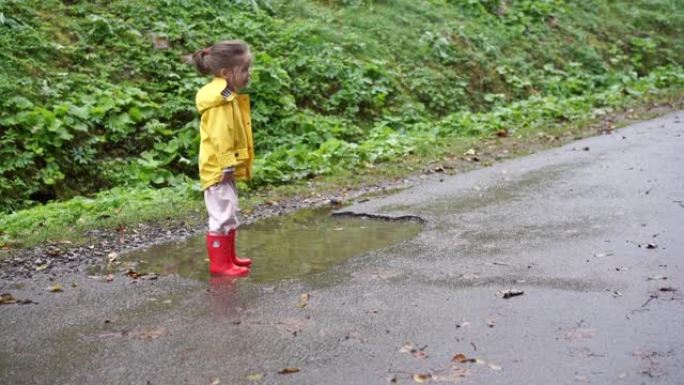 秋雨过后，孩子们穿着黄色雨衣行走水坑。小女孩泼脏水红色橡胶靴