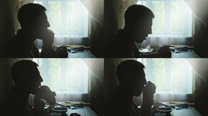 苏联士兵在参加第二次世界大战前坐在家里靠窗的地方抽烟和喝烧瓶里的酒的侧影