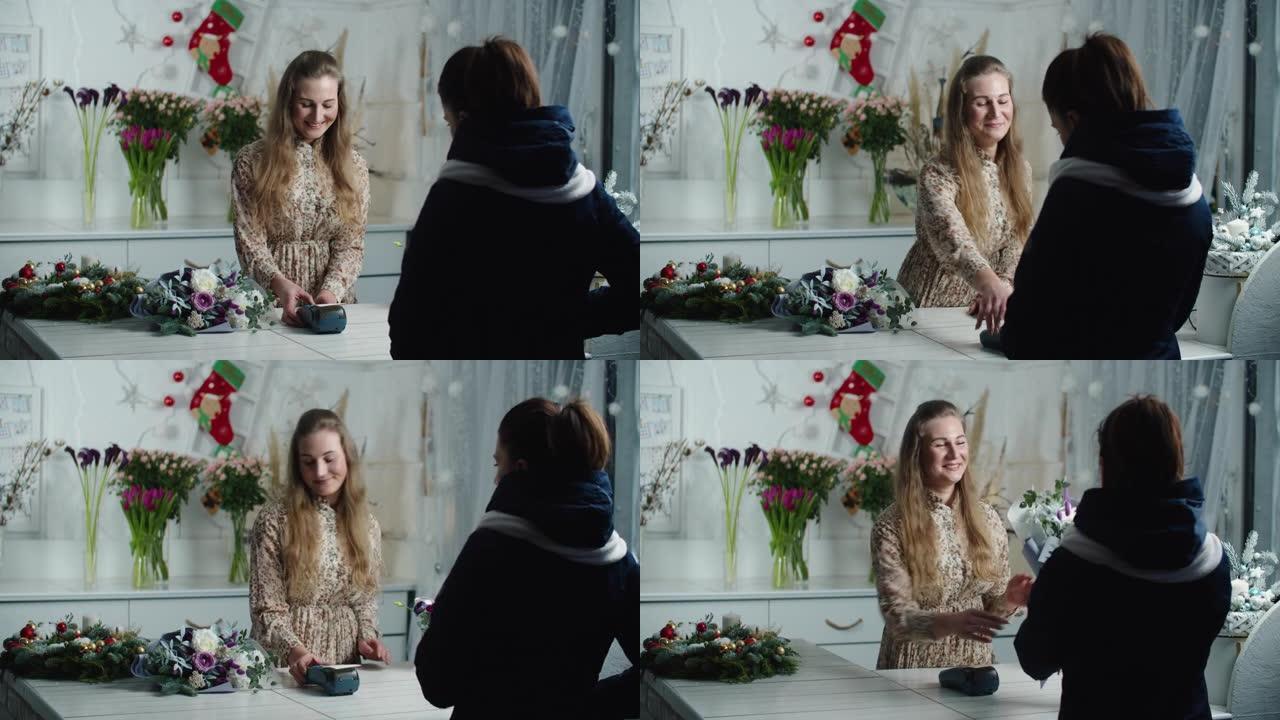 一个年轻女孩为购买一束鲜花买单。一个美丽的微笑女孩正在用信用卡支付购买鲜花作为礼物给年轻女子卖花的礼