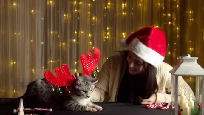 戴着圣诞老人帽子的时尚快乐女孩和可爱的猫玩耍
