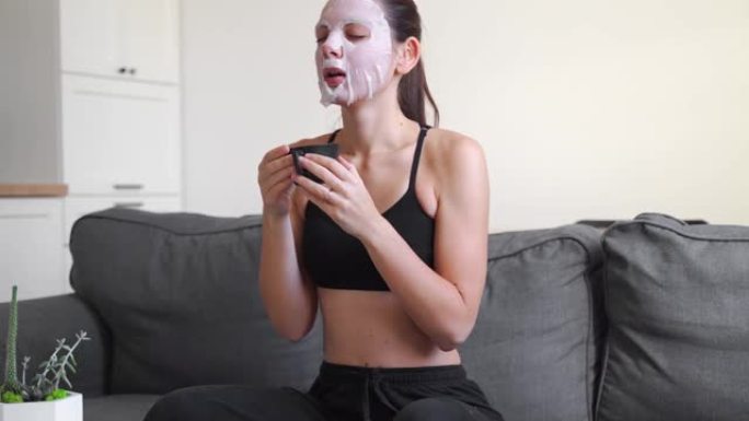 年轻的千禧一代妇女在家在脸上涂布面膜并使用电话。健康放松时间
