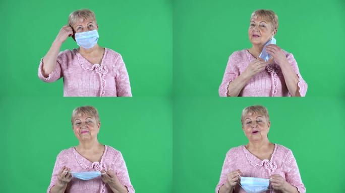 肖像老年妇女看着相机，取下医用口罩。在工作室的绿色屏幕上，白发祖母，短发穿着粉红色的毛衣。特写