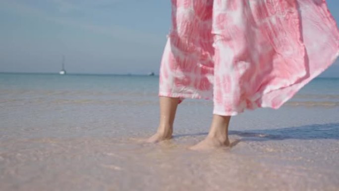 晴天，女性弯腰在白色沙滩上捡起蛤壳的镜头。年轻漂亮的女孩玩海沙水和海浪。暑假。低摄像机角度，慢动作风
