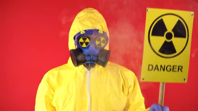 一个穿着化学防护服的男人，戴着带有辐射海报的防护面具。隔离，工作室拍摄。红色背景上的辐射危害概念。周
