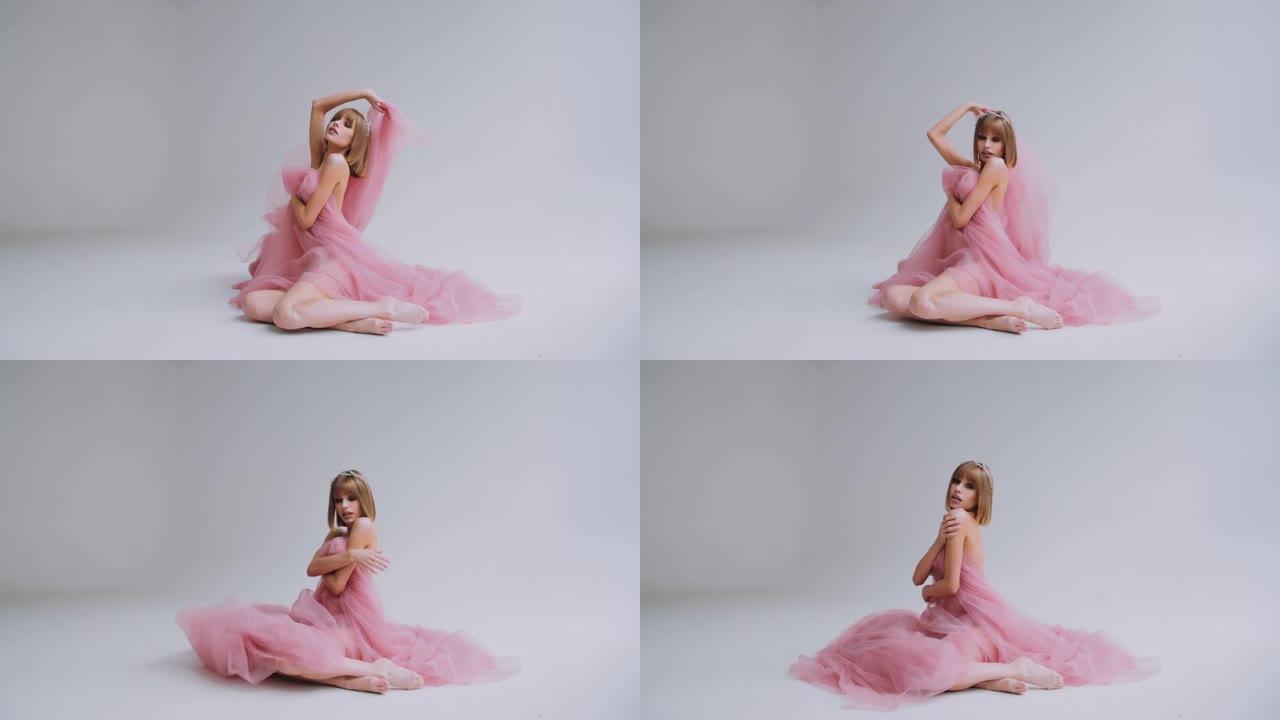 穿着粉红色飘动连衣裙的鲍勃发型的年轻女子坐在地板上。