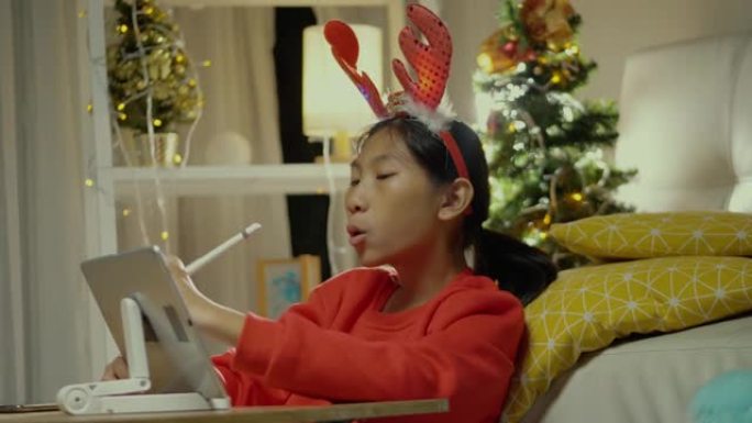 快乐的亚洲女孩穿着红色毛衣，在家里用圣诞装饰品在数字平板电脑上唱歌和绘画，生活方式概念。