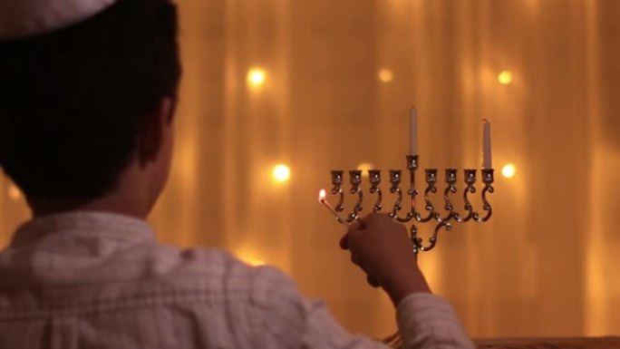 在光明节犹太节日期间，一个小男孩的视线照亮了烛台的第一支蜡烛。