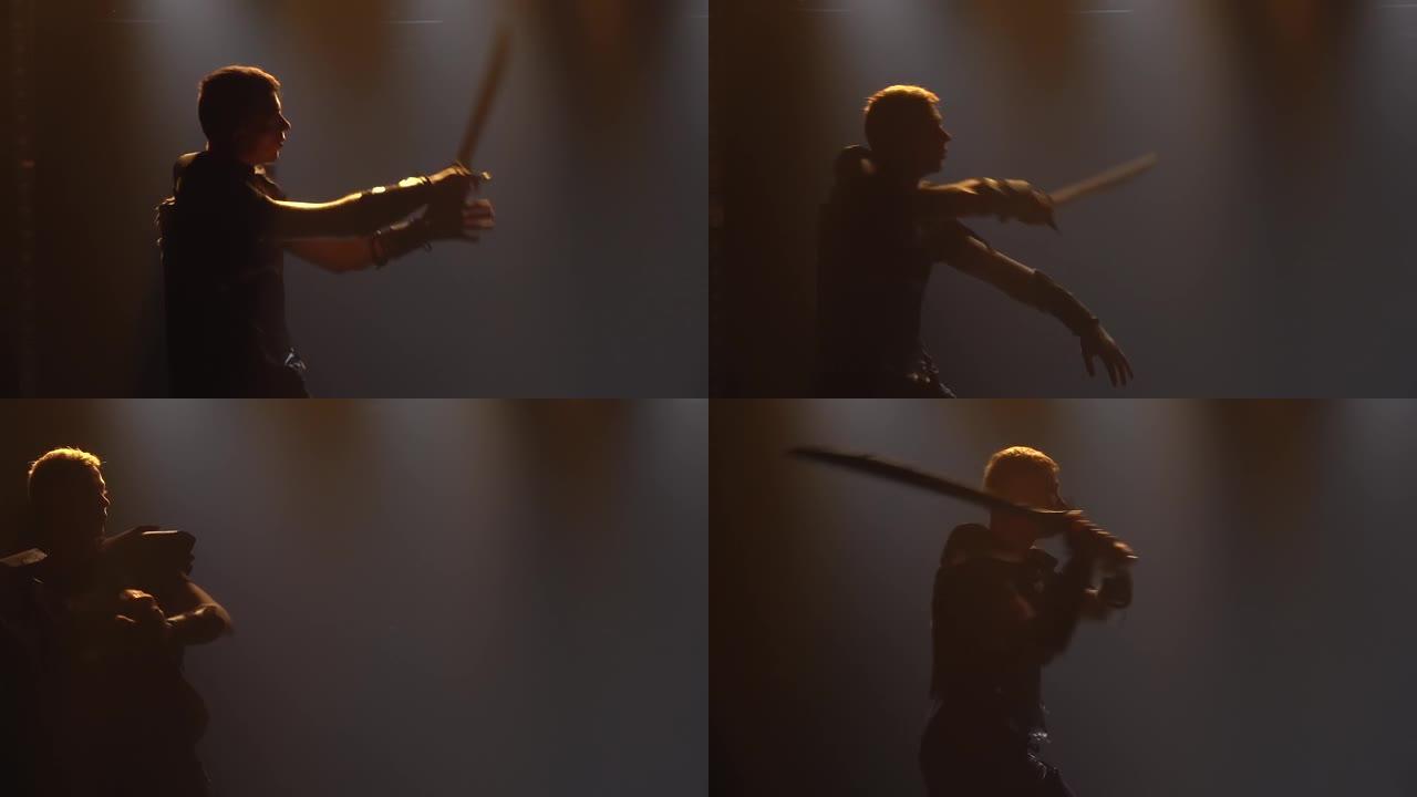 男人在带有舞台灯光的黑暗工作室里用剑战斗。在戏剧表演中穿着盔甲的男演员的剪影。慢动作特写