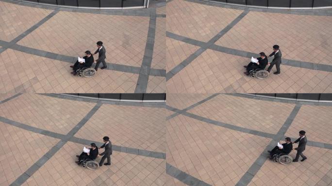 两个商人在公司大楼附近的户外聊天。同事坐在轮椅上。鸟瞰图。从顶部看。
