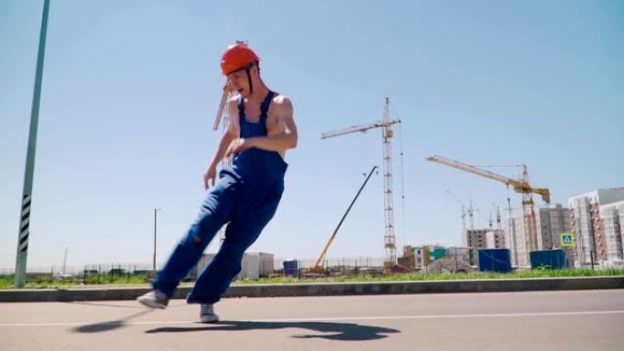 快乐的白人男子建造者戴着安全帽跳舞刹车。工人在建筑工地的背景下滑稽动作。慢动作。斯蒂安卡姆射击。