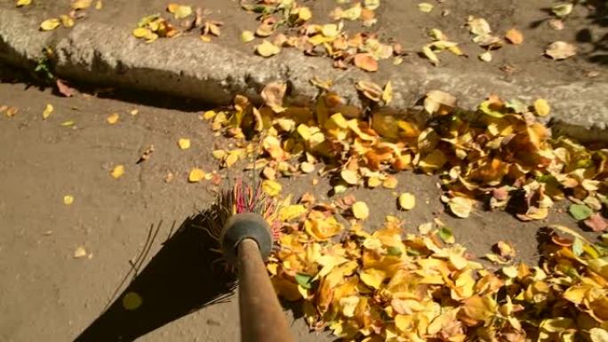 扫帚扫除道路上的黄色叶子。