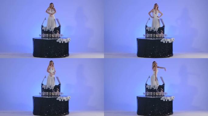梅林·门罗的图像中迷人的年轻女子在一个黑色蛋糕上跳舞。金发女郎在工作室里摆着淡蓝色的姿势。节日舞台剧