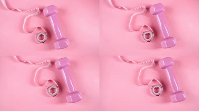 粉色背景上有哑铃和测量胶带的健身概念