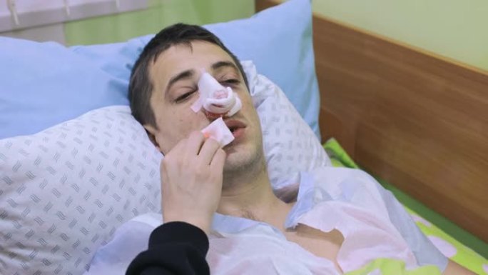 丈夫鼻子整形手术后，妻子给他干燥的嘴唇补水。