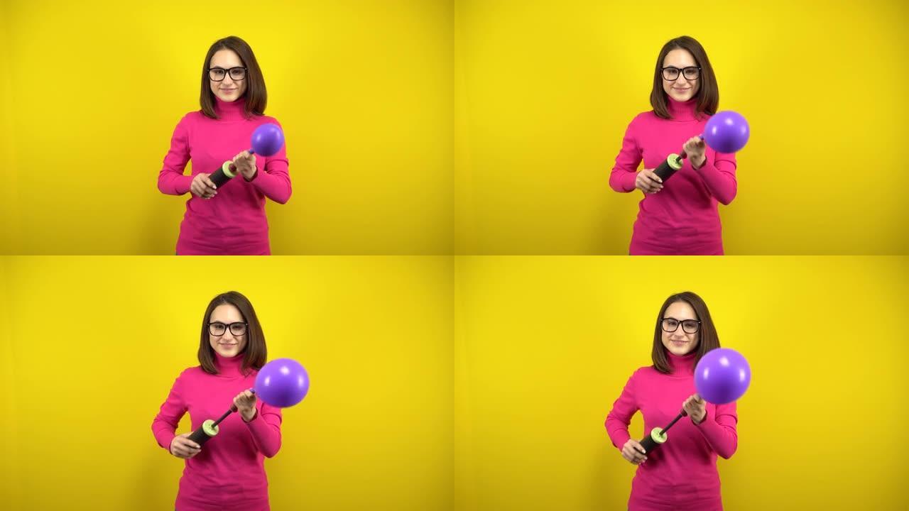 一名年轻女子用黄色背景上的泵给紫色气球充气。穿着粉色高领毛衣和眼镜的女孩。